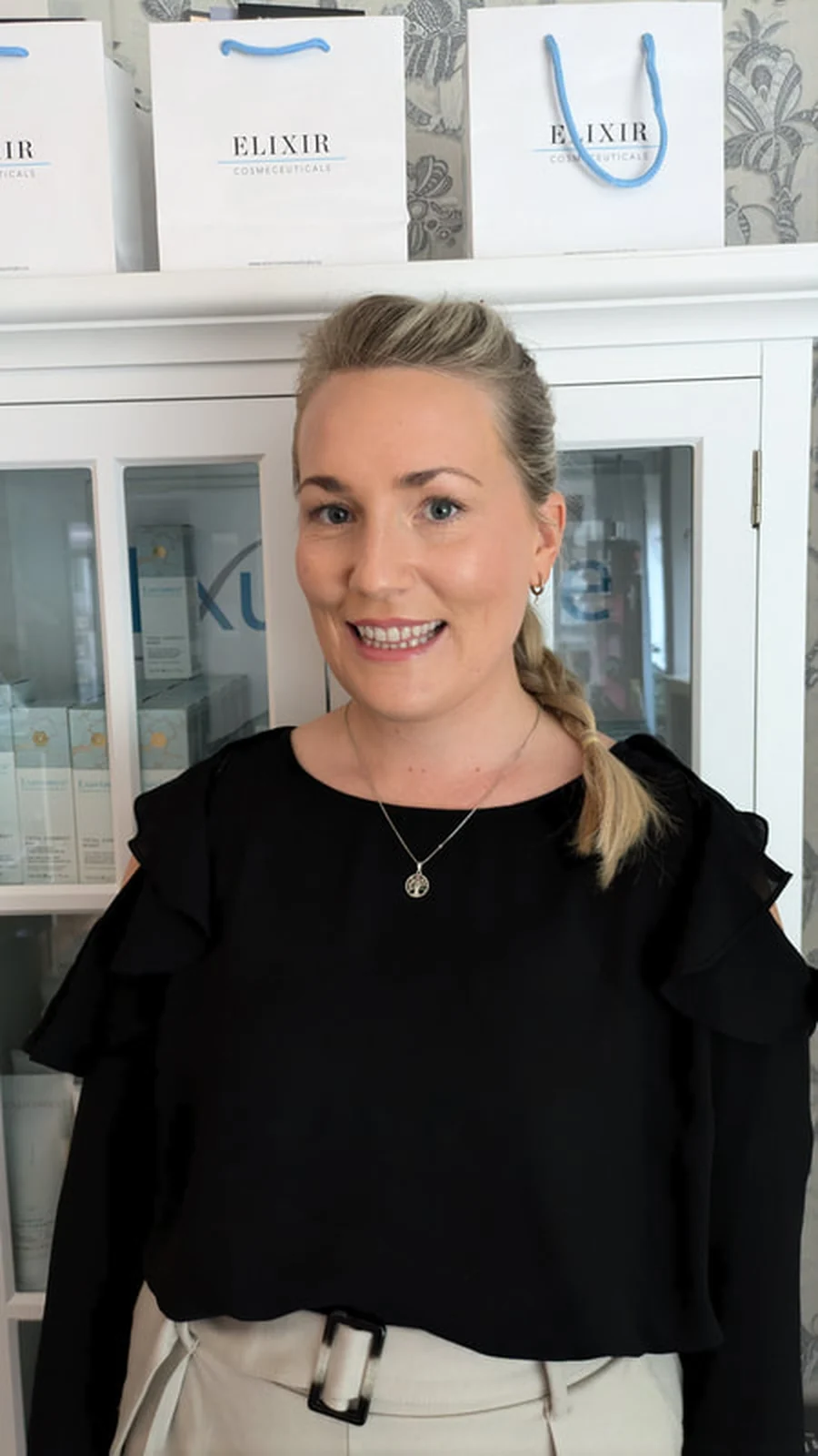 Terapeut i klinikken foran hyllene med Elixir Cosmeceuticals-produkter